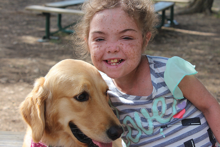 A girl with her face painted and smiling next to a dog.