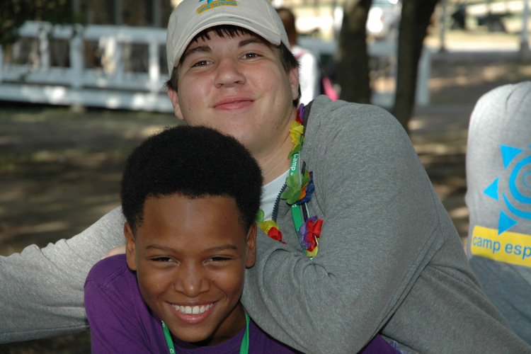 Two boys smiling for the camera while sitting on a bench.