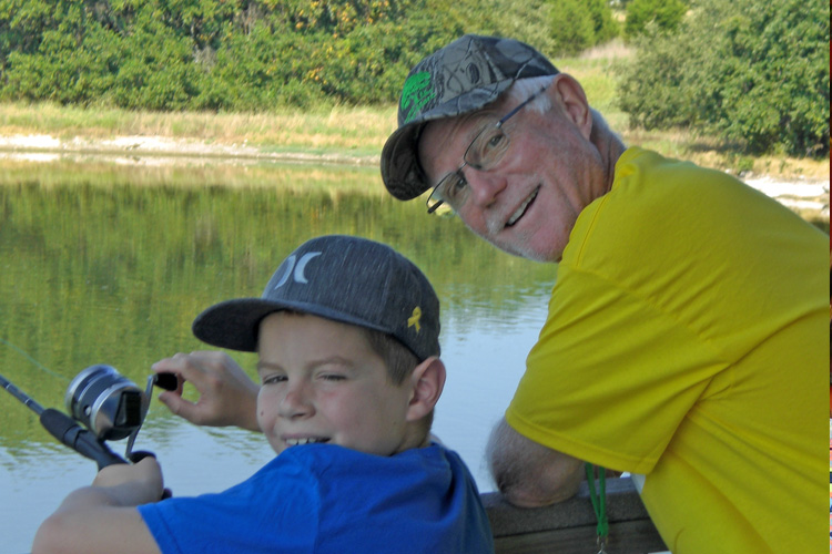 A man and boy sitting on the dock of a lake.