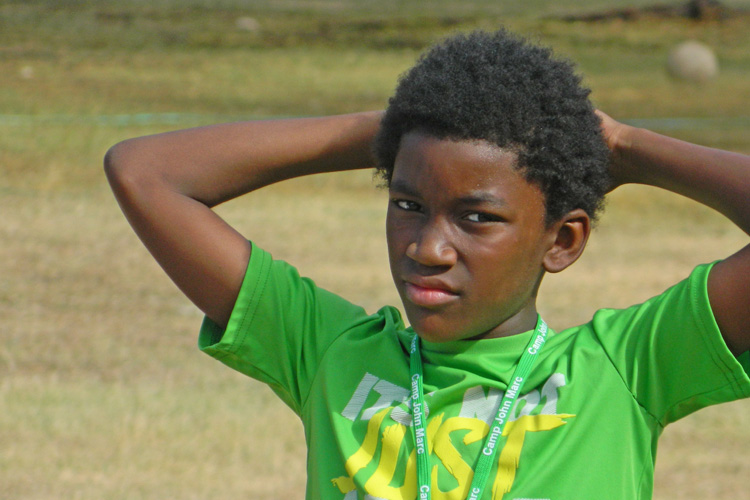 A young boy in green shirt with his hands behind head.