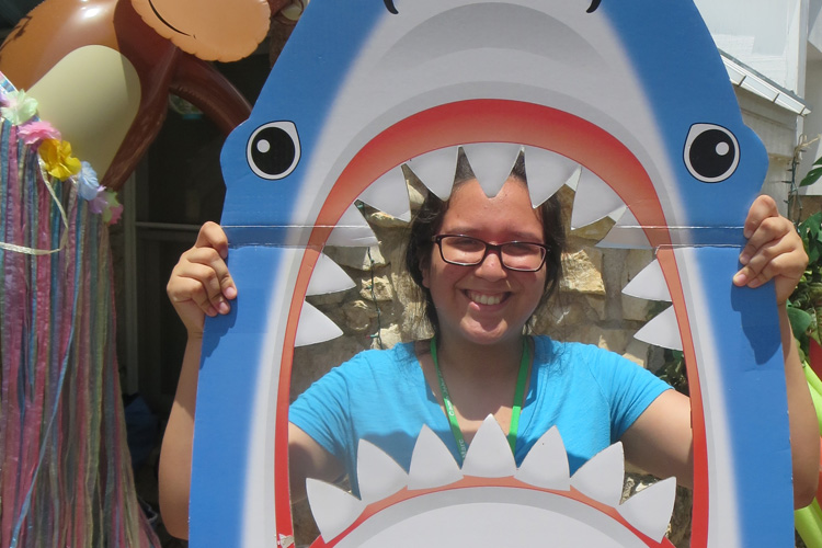 A woman is smiling while holding up a shark costume.