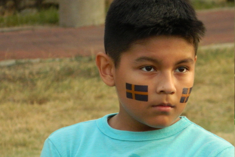 A young boy with his face painted in the colors of sweden.