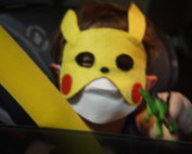 A boy wearing a pikachu mask and holding a toy.