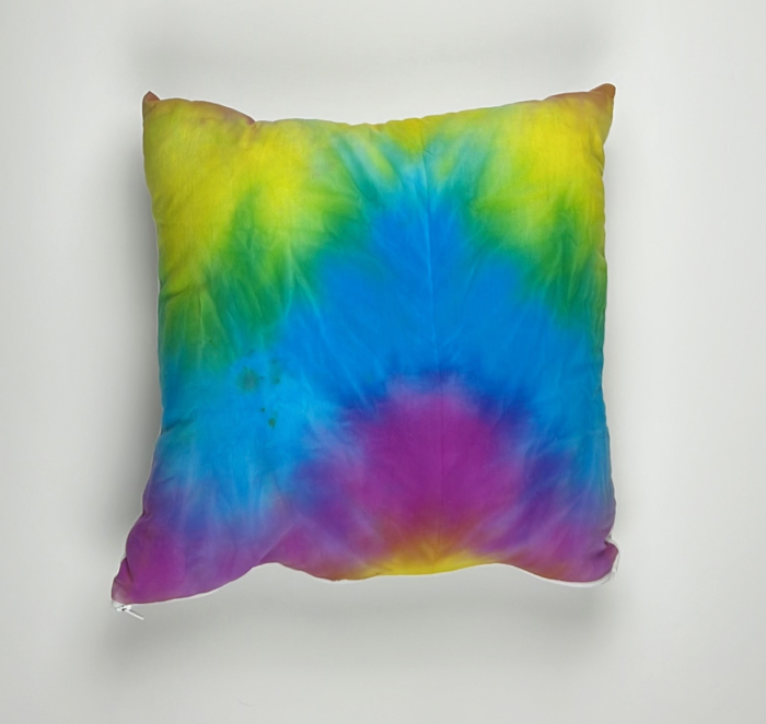 A colorful tie dye pillow on a white wall.