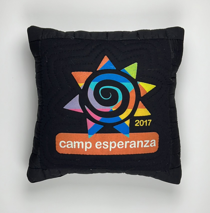 A black pillow with a camp esperanza logo on it.